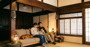 愛犬と一緒に泊まれる古民家宿のリビングで、ソファに座ってリラックスしている3人家族とダックスフンド。温かい光に包まれたノスタルジックな雰囲気。