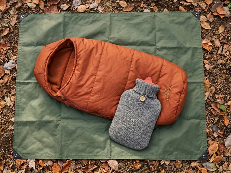 愛犬の冬キャンプ用防寒グッズ。落ち葉の上に敷かれたシートに乗る犬専用シュラフ(寝袋)とカバー付きの湯たんぽ。